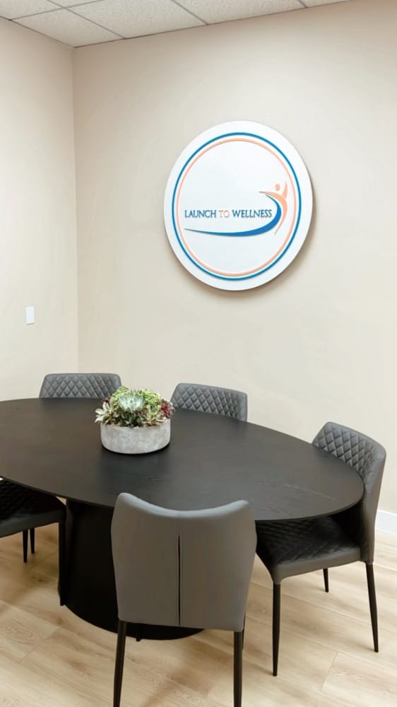 Group room with an oval table, chairs, and the Launch To Wellness wall sign