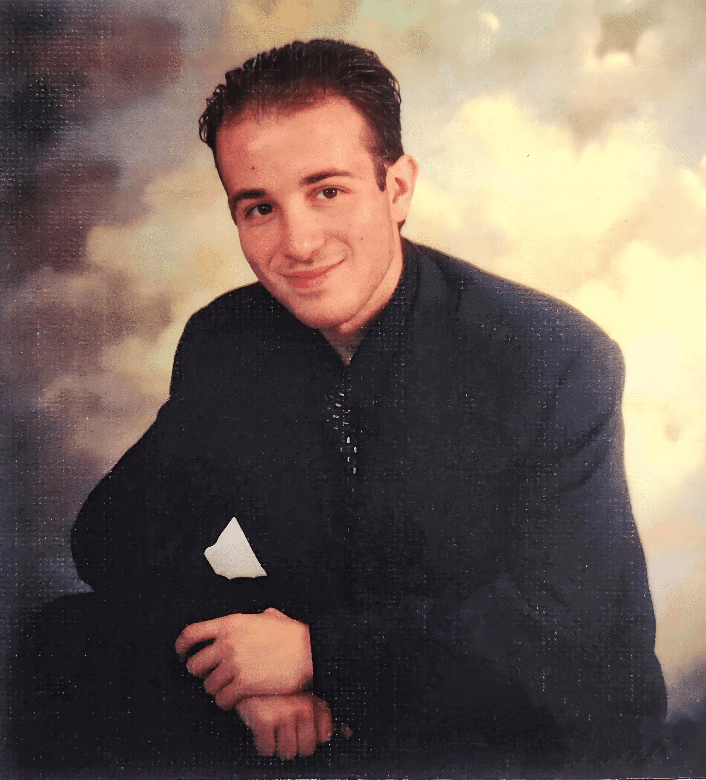 George Agabekyan seated in a dark suit, smiling, against a painted sky.