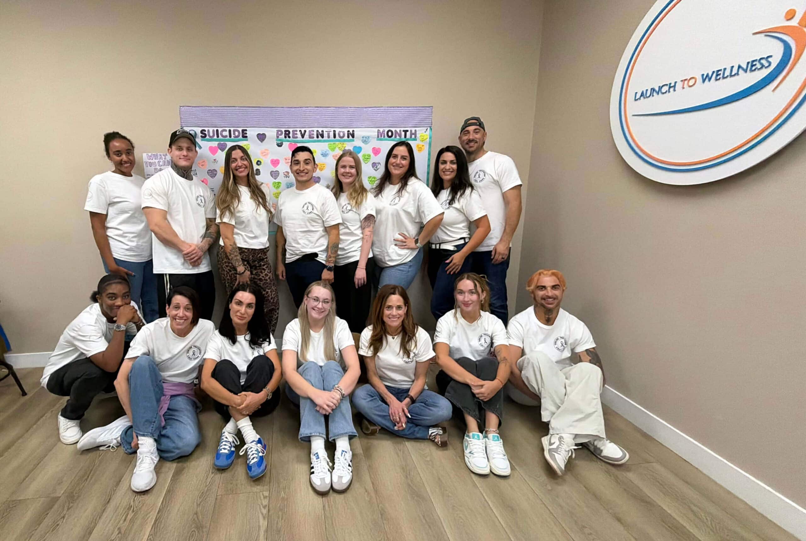Launch To Wellness team gathered indoors at the Woodland Hills center, wearing white shirts beside the Launch To Wellness wall logo